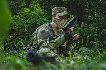 the military sits on the grass and examines his gun