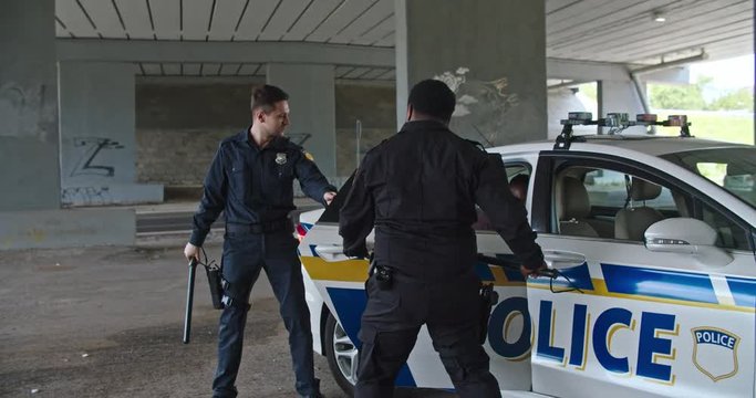 Fun scene at arrest. Joyful positive police officers let out a robber encourage him to dance with cool moves together near the patrol car.