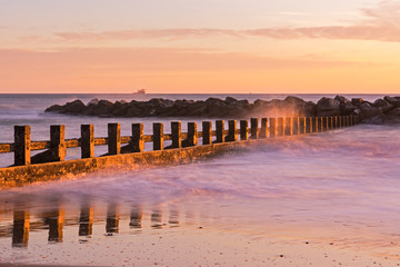 Sunrise at Aberdeen Beach in Scotland. Waves crashing into wooden panels in the water. Beautiful pink sky. Orange, pink color in the sky. Amazing seascape.