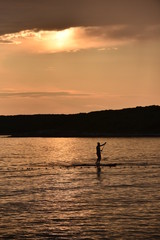 Person using a sup in the sunset.