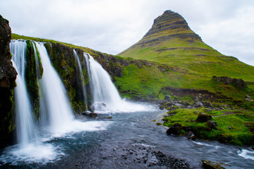 Scenic panorama view of long exposure falling water in front of Kirkjufell volcano mountain, the most iconic travel destination location in Iceland. Summer time.
