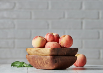 Peaches in wooden bowl with white brick wall background