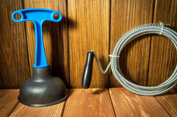Clean plastic plunger with blue handle, pipe wrench and cable on wooden background.