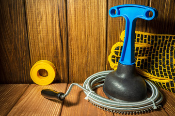 Clean plastic plunger with blue handle, pipe wrench and cable on wooden background.