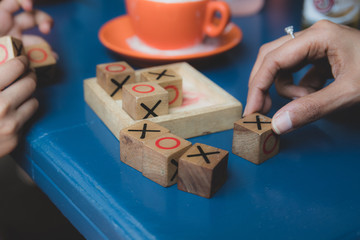 A set of wooden naughts and crosses in a blue table with parent and child fingers playing it during summer holidays at a cafe. 