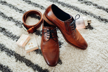 Groom's wedding day accessories. Brown leather shoes, belt, perfume, golden rings. Male fashion