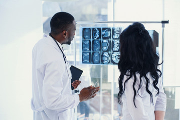 Two doctors are looking at x-rays. Medical. Rear view of chief physician afro american man and caucasian woman looking at an x-rays MRI at clear light