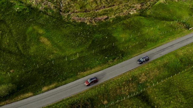 Two SUVs drive one after another along country road in field. Aerial view.