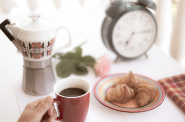 Close up of human hand taking a red cup of coffee. Relaxed moment before working day. Big old alarm clock. Old coffee pot and a rose on background