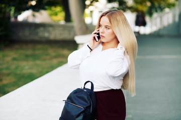 Fototapeta premium Young stylish woman wearing neutral blazer and hat walking on the city street in spring. Casual fashion, elegant look. Plus size model.