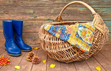 Fototapeta na wymiar Rubber boots and wicker basket closeup. Hike for mushrooms in the forest. Autumn concept.