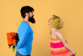 Couple, relationships and people concept. Presents on womens day. Surprise for girl. Man hiding flowers and gift for his girlfriend behind his back. Valentine day. Romantic man with present for woman.