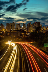 Fototapeta na wymiar Trail of light caused by vehicular traffic in SP-294, Comandante Joao Ribeiro Barros Highway with buildings from downtown in the background, in Marília, during a late afternoon.