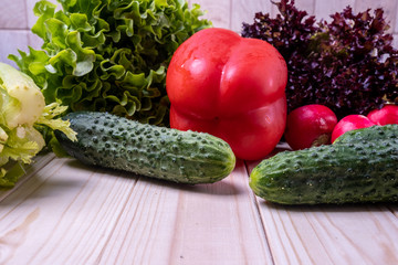 fresh vegetables on a light wooden table, paprika, celery, leaves of lettuce, cucumbers and radishes