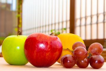 Green and red apples next to an orange and some grapes
