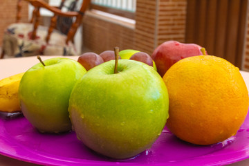 Several wet fruits on a purple tray