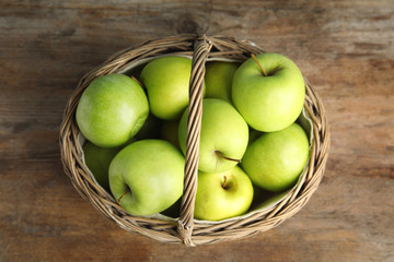 Wicker basket of fresh ripe green apples on wooden table, top view