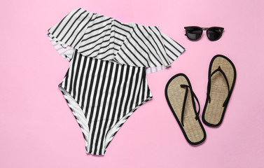 Flat lay composition with striped swimsuit and beach accessories on pink background
