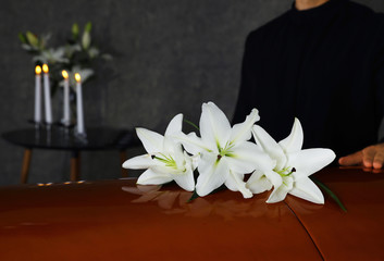 Fototapeta na wymiar Young man near casket with white lilies in funeral home