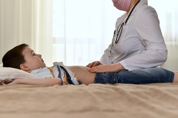 A doctor in a white coat checks the belly of a child. Sitting on the bed in the patient house. The...