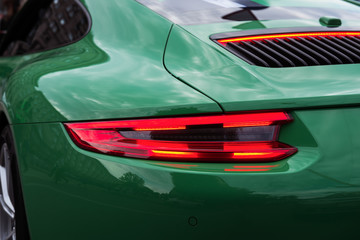 Green sports car with red backlight on. Closeup of a luxury car body. Modern LED light. Rear light...