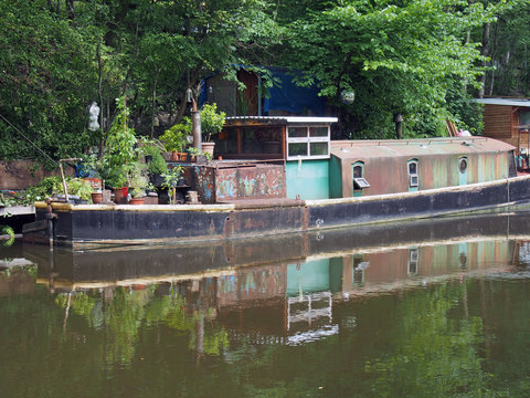 an old rusty narrow boat reflected in the water and surrounded by trees on the rochdale canal in hebden bridge west yorkshire