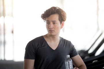 Interesting young man resting drinking water after practicing running at the running machine At the gym, fitness concept