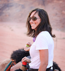 White woman rides a camel in the desert of Wadi Rum, Jordan. 