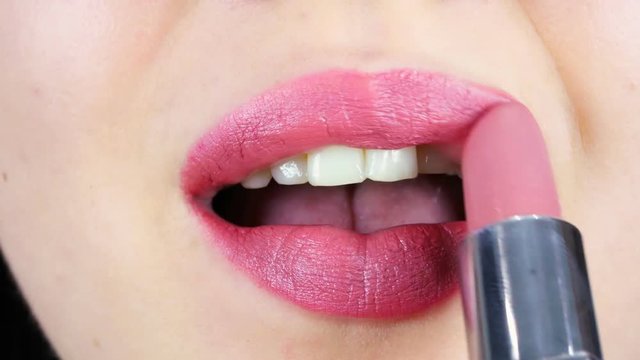 Extreme close-up of lips of a young woman. Woman paints lips with lipstick for makeup. Women's morning makeup
