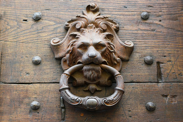 Alter Türklopfer aus Metall als Löwenkopf an einer rustikalen Holztür in Italien