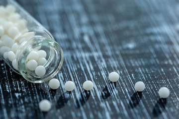 Still life concept of homeopathic pills with homeopathy granules on a grey wooden background - obrazy, fototapety, plakaty