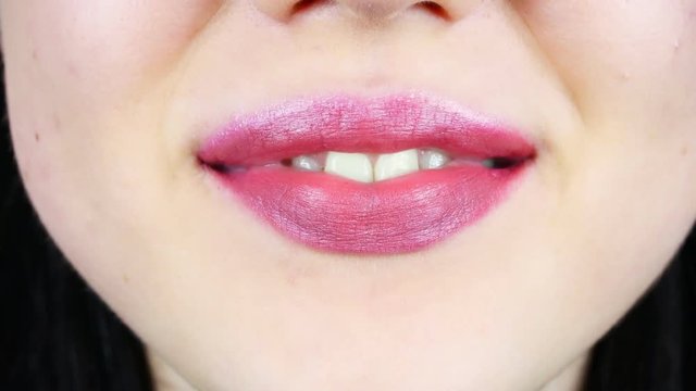 Extreme close-up of lips of a young woman. Woman paints her lips with bright lipstick for makeup. Women's morning makeup