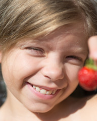 Portrait of cute blonde Caucasian girl is holding a red berry in her hand. Girl is smiling