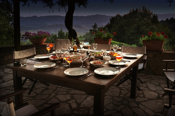 large rustic table on a garden terrace prepared for a dinner party at night