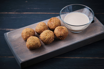 Classic hummus balls with thin sauce on a wooden board on a dark wooden background. National, vegetarian dish.