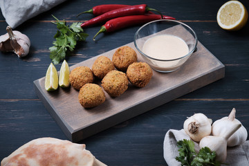 Classic hummus balls with thin sauce on a wooden board on a dark wooden background. National, vegetarian dishes and ingredients.