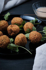 Classic balls of hummus with thina sauce in a plate on a wooden table. National, vegetarian dish, ingredients and cilantro.