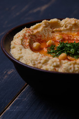 Classic hummus with hot pepper in a clay plate on a wooden table. National, vegetarian dish. General form.
