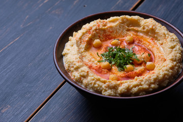 Classic hummus with hot pepper in a clay plate on a wooden table. National, vegetarian dish. General form.
