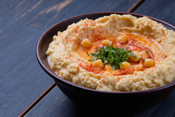Classic hummus with hot pepper in a clay plate on a wooden table. National, vegetarian dish. General form.