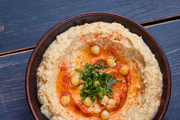 Classic hummus with hot pepper in a clay plate on a wooden table. National, vegetarian dish. General form.