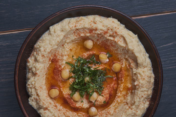 Classic hummus with hot pepper in a clay plate on a wooden table. National, vegetarian dish. General form.