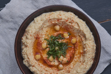 Classic hummus with hot peppers in a clay plate on a linen towel. National, vegetarian dish. General form.
