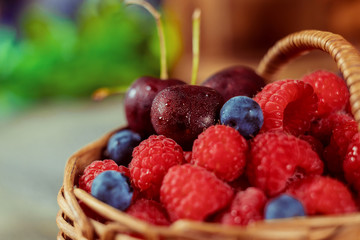 Raspberries and blueberries in a basket with handle and couple cherries