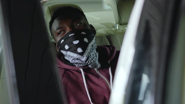 African american offender in mask sitting in patrol car in handcuffs burglar crime hold danger gangster gun robber security dangerous handgun illegal law outlaw arrest bad guy close up slow motion