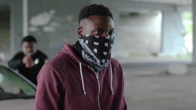Young african american offender in mask stand in patrol car in handcuffs burglar crime hold danger gangster gun robber handgun illegal law outlaw arrest bad guy close up slow motion