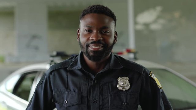 Smiling face african american young man cops stand near patrol car look at camera enforcement happy officer police uniform auto safety security communication control policeman portrait slow motion