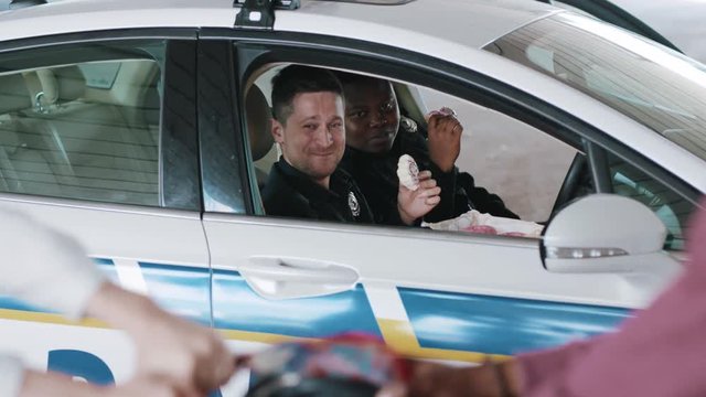 Portrait two policemen eating donut smile talk see how a man steals a woman's bag near patrol car help happy african american break rest gangster uniform funny teamwork slow motion