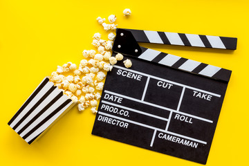 Watch film in cinema with popcorn and clapperboard on yellow background top view
