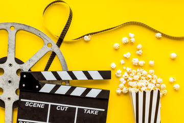 Watch film in cinema with popcorn, video tape and clapperboard on yellow background top view